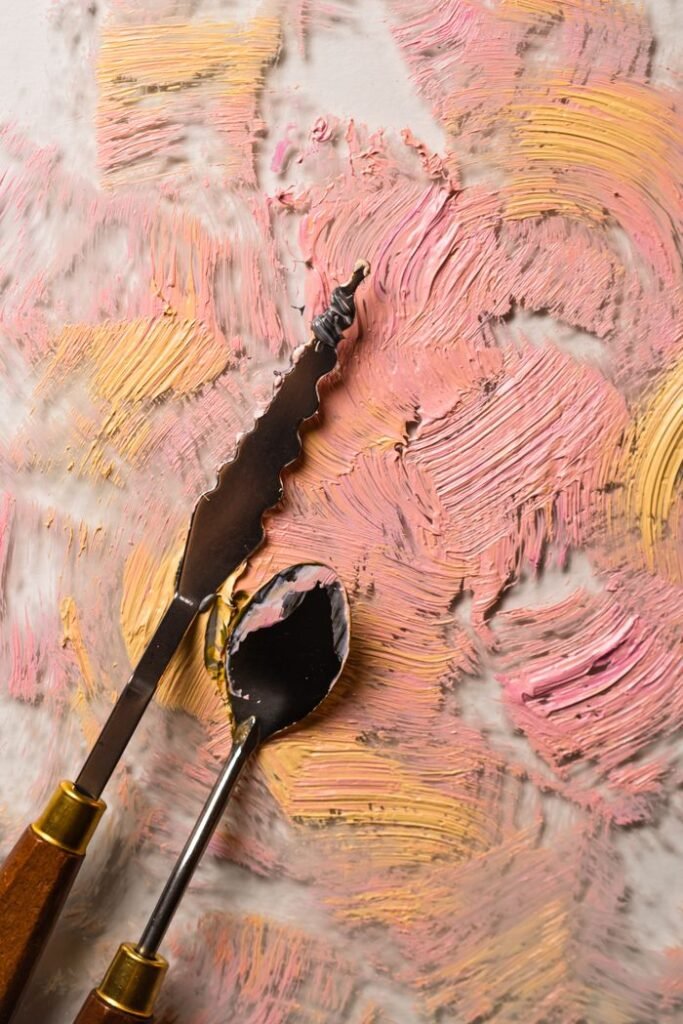 Close-up of abstract knife painting with textured pink and yellow patterns using palette knives.