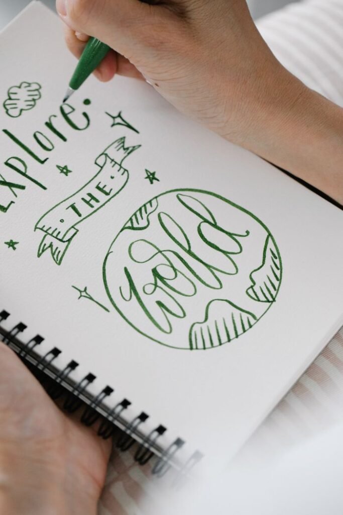 Close-up of a hand drawing inspiring calligraphy art in a notebook with a green pen.